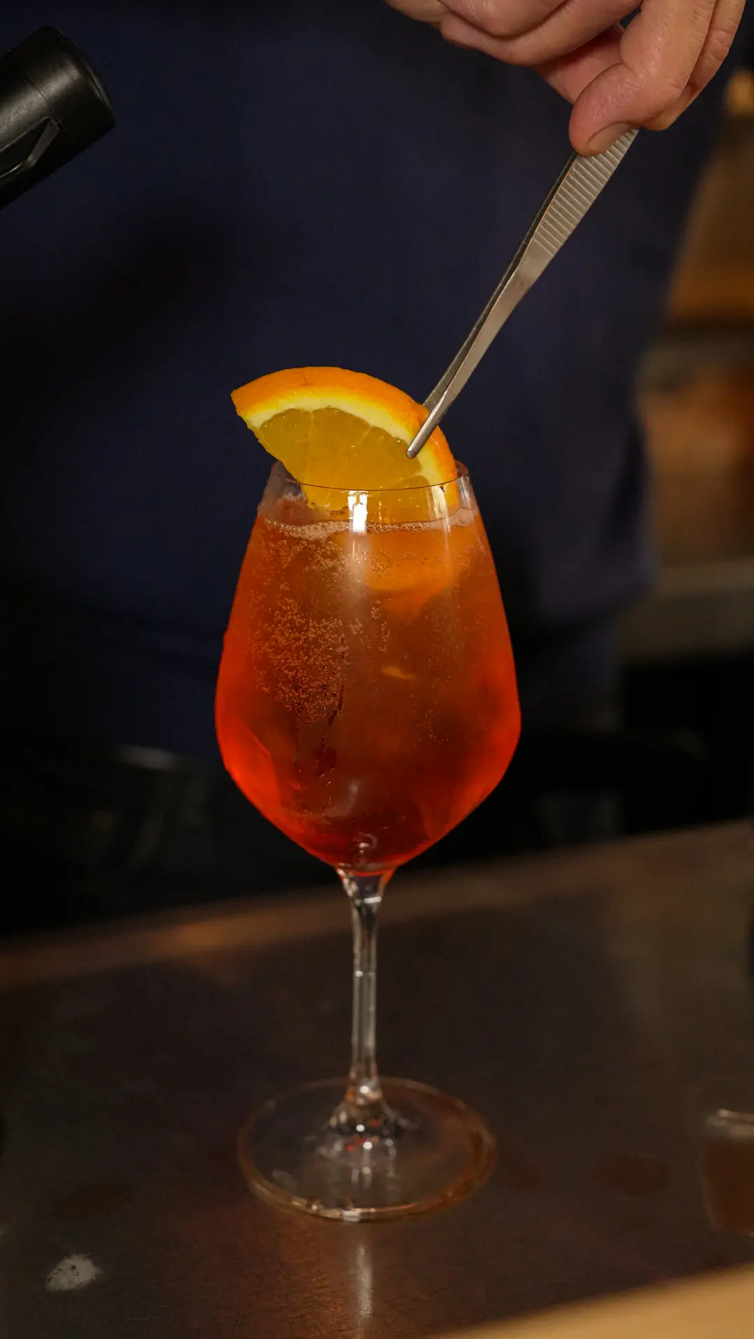 Un spritz garni d'une tranche d'orange, préparé au comptoir.