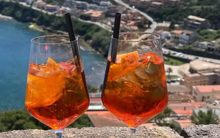 Deux spritz posés sur un muret, face à la mer et à un village italien.